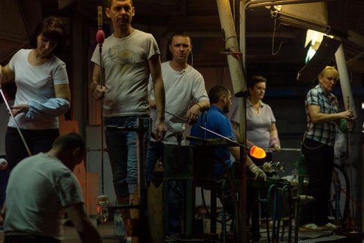 Beryozauka, Belarus - March 07, 2022: A team of glass blowers is working on the manufacture of glass vases and glasses. Up to 20 workers can be involved simultaneously in the production of particularly complex products.
