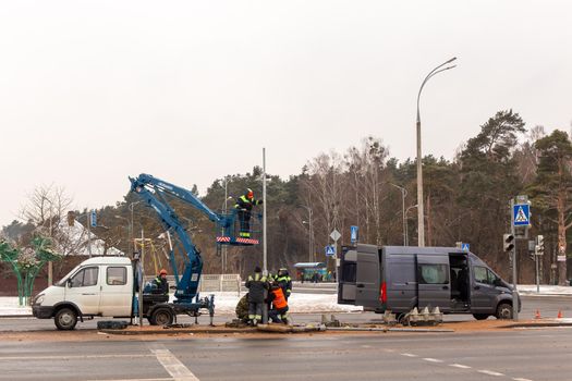 Grodno, Belarus - December 23, 2021: A team of workers is repairing a traffic light that was broken as a result of a traffic accident. Workers use a car-based lift.