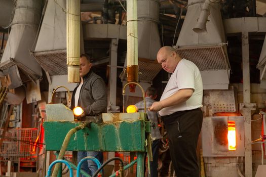 Beryozauka, Belarus - March 07, 2022: A team of glass blowers is working on the manufacture of glass vases and glasses. Up to 20 workers can be involved simultaneously in the production of particularly complex products.