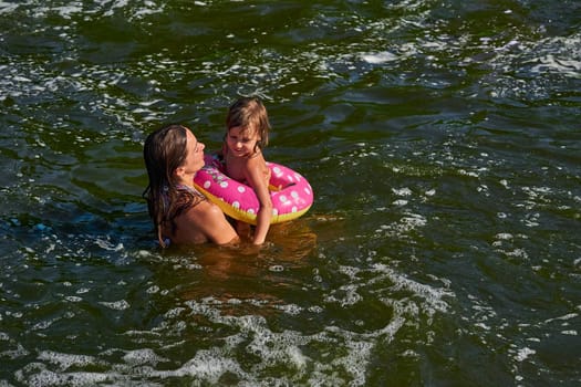 propel the body through water by using the limbs,by using fins, tail, or other bodily movement.Cute girl on a swimming circle bathes with her mother protecting her in the sea.