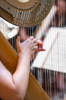 harp on symphony orchestra stage, detail of hands with strings.