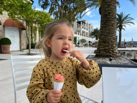 Little girl eating ice cream with a spatula at the table. High quality photo