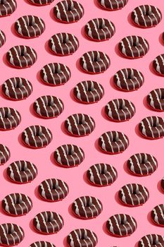 Concept food design with tasty chocolate glazed donut with white strips on coral pink pastel background top view pattern. Mock up, flat lay style