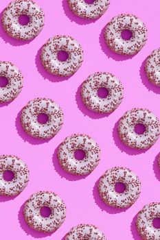 Concept food design with tasty pink glazed donut with red flakes on purple lilac pastel background top view pattern. Mock up, flat lay style