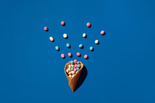 Flat lay photo of a heap of candy dragee that is sprinkled from a waffle cone on blue background from above