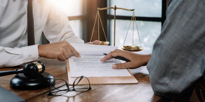 client customer signing contract and discussing business with legal consultants, notary or justice lawyer with laptop computer and wooden judge gavel on desk in courtroom office, legal service concept.