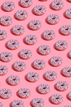 Concept food design with tasty pink glazed donut with red flakes on coral pink pastel background top view pattern. Mock up, flat lay style