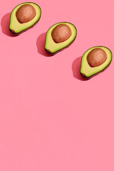 Food design. Top view of colorful fruit pattern of fresh cutted avocado halves with pits inside on coral pink pastel background. Mock up, flat lay style.