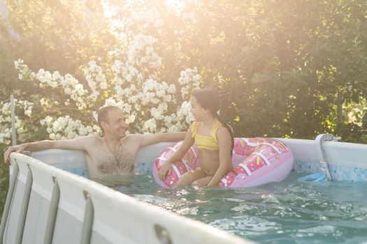 The father with little daughter have fun in the pool. Dad plays with the child. The family enjoy summer vacation in a swimming pool jumping, spinning, splash water