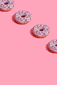 Concept food design with tasty pink glazed donut with red flakes on coral pink pastel background top view pattern. Mock up, flat lay style