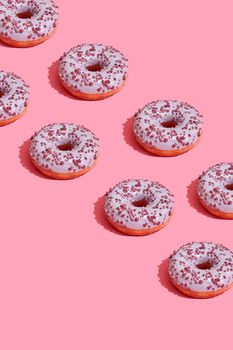 Concept food design with tasty pink glazed donut with red flakes on coral pink pastel background top view pattern. Mock up, flat lay style