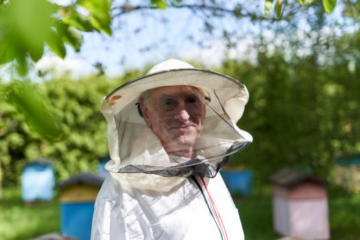 Close up portrait of a smiley beekeeper with protective gear in a farm with beehives