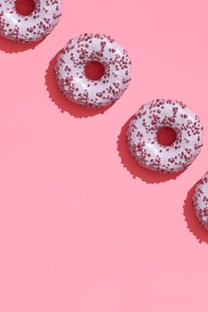 Concept food design with tasty pink glazed donut with red flakes on coral pink pastel background top view pattern. Mock up, flat lay style