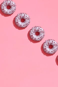 Concept food design with tasty pink glazed donut with red flakes on coral pink pastel background top view pattern. Mock up, flat lay style