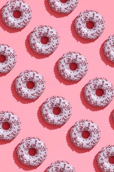 Concept food design with tasty pink glazed donut with red flakes on coral pink pastel background top view pattern. Mock up, flat lay style