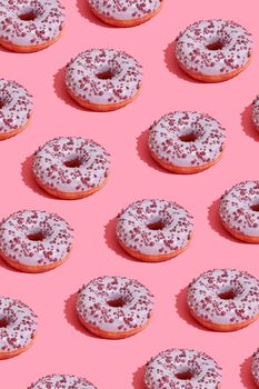 Concept food design with tasty pink glazed donut with red flakes on coral pink pastel background top view pattern. Mock up, flat lay style