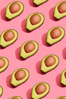 Food design. Top view of colorful fruit pattern of fresh cutted avocado halves with pits inside on coral pink pastel background. Mock up, flat lay style.