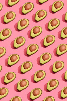 Food design. Top view of colorful fruit pattern of fresh cutted avocado halves with pits inside on coral pink pastel background. Mock up, flat lay style.