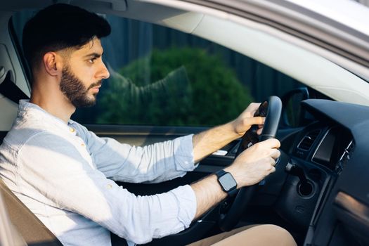 Businessman holding steering wheel while driving modern electric car on the street road. Confident man driving expensive car. Driver Turning Steering Wheel In Luxurious Auto On Trip.