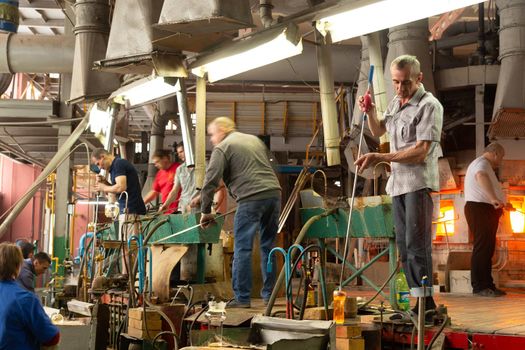 Beryozauka, Belarus - March 07, 2022: A team of glass blowers is working on the manufacture of glass vases and glasses. Up to 20 workers can be involved simultaneously in the production of particularly complex products.