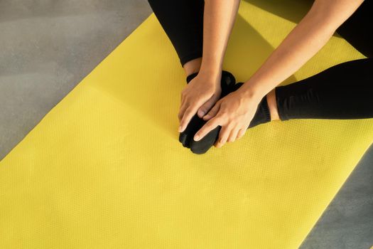 Girl does stretching on yoga mat, her legs are folded in butterfly pose and her hands hold feet, close-up. Concept of healthy lifestyle. Copy space
