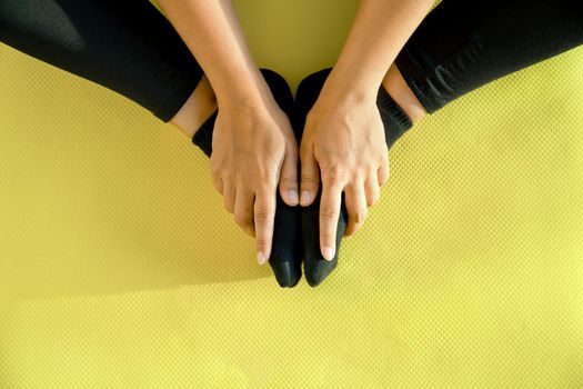 Girl does stretching on yoga mat, her legs are folded in butterfly pose and her hands hold feet, close-up. Concept of healthy lifestyle. Copy space