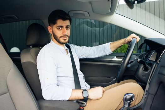 Attractive elegant happy man in good car. Confident businessman driving an expensive car and loking at camera