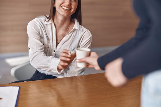 Happy woman is taking a paper cup from receptionist in modern dental clinic
