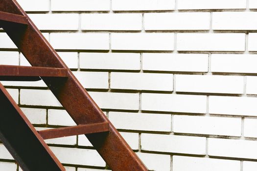 a structure consisting of a series of bars between two upright lengths of wood, metal used for climbing up or down.Part of the stairs red metal ladder leading up against of a white brick wall