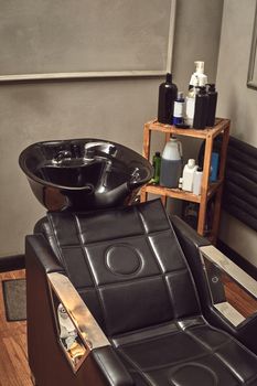 Black leather seat with wash basin in a barbershop interior with towels and shampoo on the side. Fashionable haircut from a professional