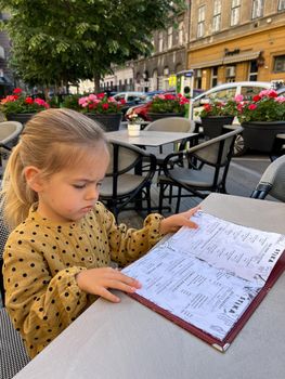 Little girl reads a menu at a table in an open-air restaurant. High quality photo