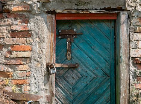 A green wooden door in an old brick barn with a metal hanging lock.