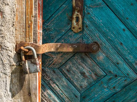 Close up of sliding bolt. Old rusty lock and latch on worn green wooden door.