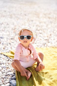 Little girl in sunglasses and panama sits on the beach. High quality photo