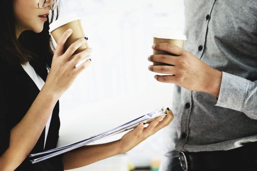 Focus on a woman's hand holding a cup of coffee and chatting with a coworker during the afternoon break