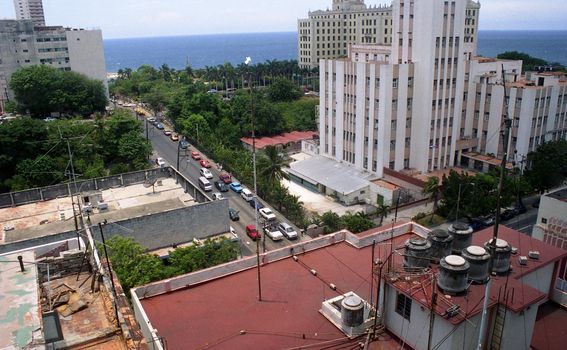 Tall Hotel buildings, Rooftops, and the street below with cars and trees stretching to the water in Havana, Cuba. 2004.