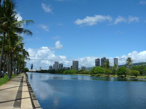 Ala Wai Canal, hotels, Condos, Golf Course and Coconut trees on a nice day in Waikiki on Oahu, Hawaii with mountains in the distance.