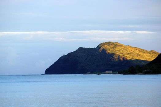 Waimanalo bay, Pier, and Makapuu Point with Makapu'u Lighthouse visible on cliffside mountain at dusk on windward coast of Oahu, Hawaii.