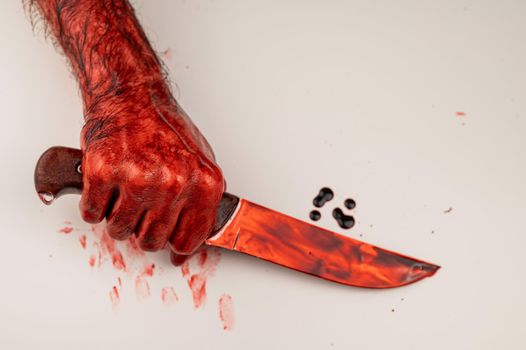 A man with bloody hands holds a knife on a white background