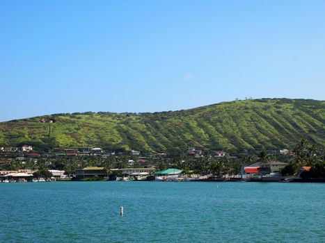 Kuapa Pond and Hawaii Kai Town Shopping buildings along the water with Hill behind it on the South East Corner of Oahu of a beautiful clear day.