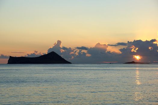 Early Morning Sunrise over Waimanalo Bay over Rock Island bursting through the clouds, Rabbit island also visible in photo.