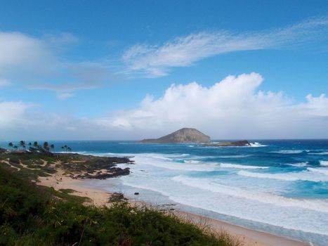 Empty beach due to large wave and view of islands on a cloud filled day at Makapuu Beach Park, Oahu, Hawaii.