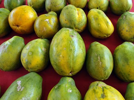 Rows of Hawaiian papayas on red cloth at a farmer's market in Hawaii.