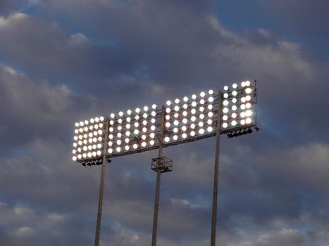 Stadium-style lights, taken at Oakland Colisuem looking forward, cloudy sky background, during the dusk so the lights are on.