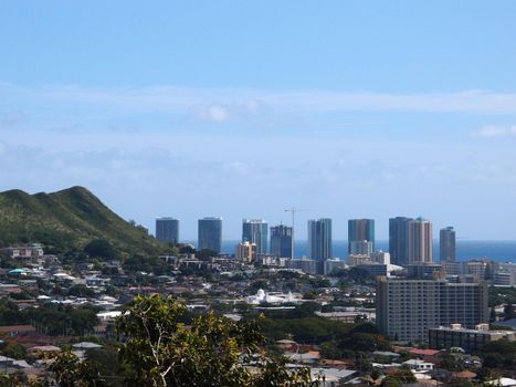 Punchbowl Crater, Nuuanu, and Honolulu Cityscape looking to the ocean from high up in the hills with cranes and modern skycrapers mixed with houses, and other small buildings.