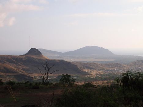 Waianae Dry Landscape with trees, mountains, town, and ocean in the foggy distance.