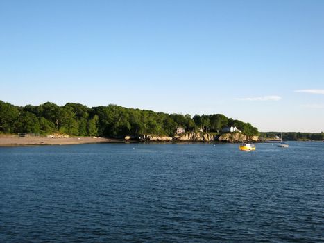 Beach, house on island shore and boats in the waters of Portland Harbor in Maine.