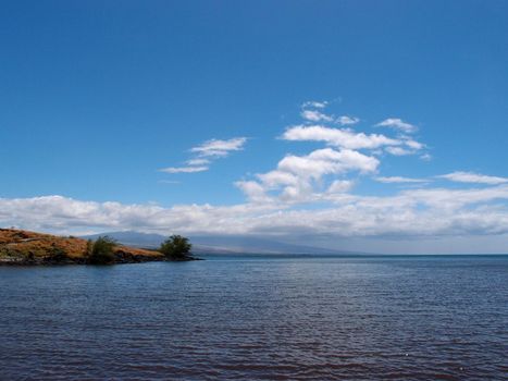 Ocean Waters and shoreline of the Kohala Coast at ancient Hawaiian historical site on the Big Island with Volcanic mountain in the distance with clouds hanging over it.