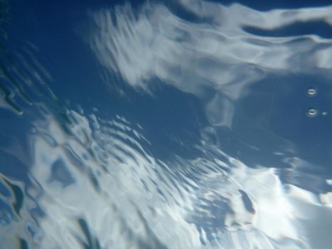 Looking through ocean water at blue sky and clouds with water ripples from underwater.