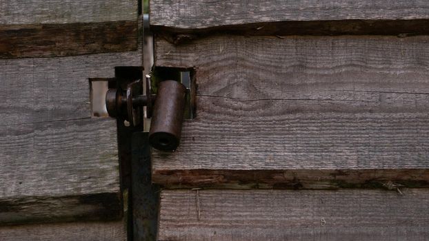 Hanging metal lock on a wooden gate. A dark metal castle in close-up in a gate made of wooden planks.